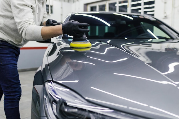 Autodetaillierung - Arbeiter mit Orbitalpolierer in der Autowerkstatt.