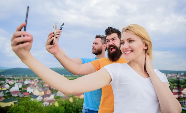 Autofoto de hoy. Mujer bonita y hombres con smartphones en las manos. La gente disfruta de la toma de selfies en el paisaje natural. Mejores amigos tomando selfie con teléfono con cámara. Compartiendo selfie en la red social.