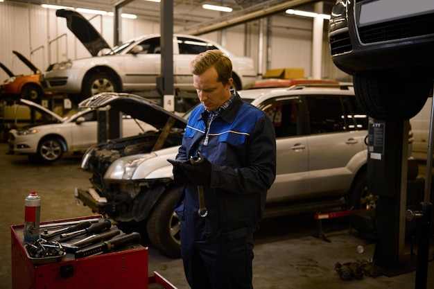 Autogarantie-Reparatur- und Wartungskonzept. Techniker, Mechaniker in professioneller Uniform mit Schraubenschlüssel in der Werkstatt.