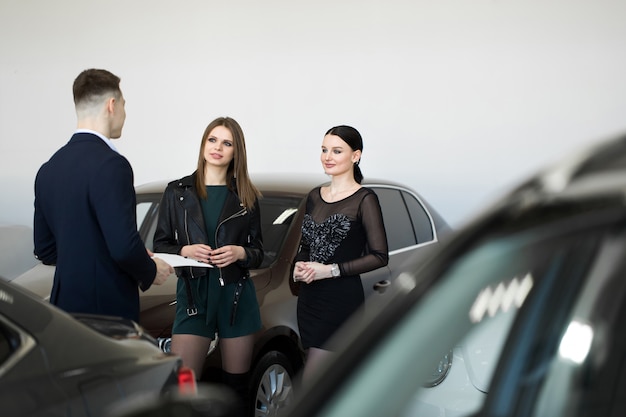 Autogeschäft, autoverkauf - ein paar freunde von mädchen mit einem autohändler wählen ein auto in einem autohaus