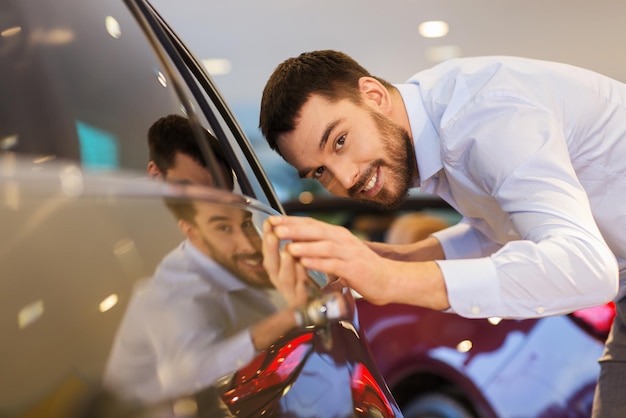 autogeschäft, autoverkauf, konsum und personenkonzept - glücklicher mann, der auto in der autoshow oder im salon berührt