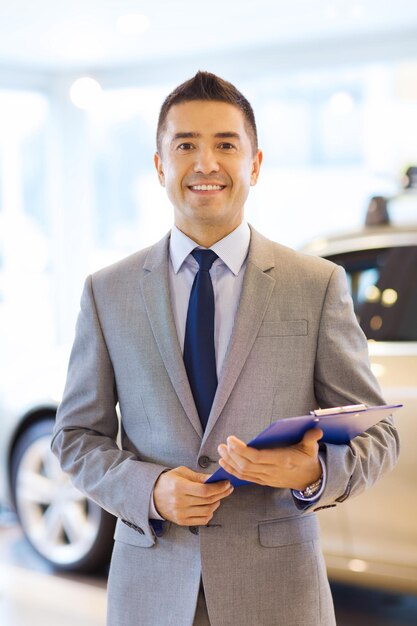 autogeschäft, autoverkauf, konsum und personenkonzept - glücklicher mann mit zwischenablage auf der autoshow oder im salon