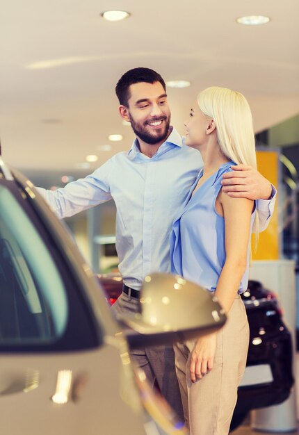 autogeschäft, autoverkauf, konsum und personenkonzept - glückliches paar, das auto in der autoshow oder im salon kauft