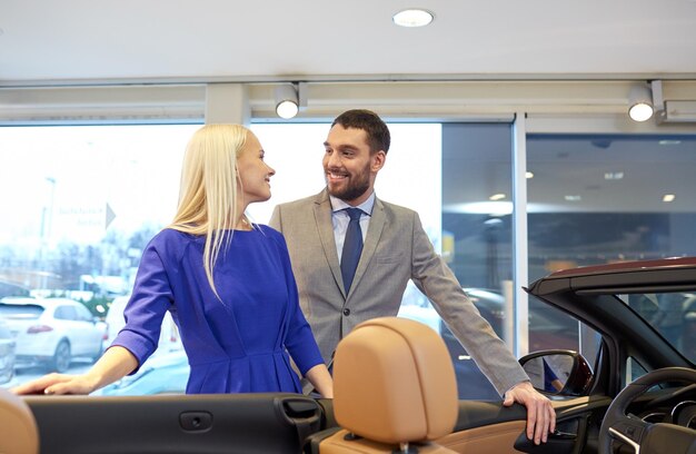 Autogeschäft, autoverkauf, konsum und personenkonzept - glückliches paar, das auto in der autoshow oder im salon kauft