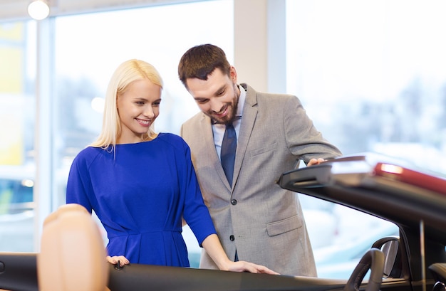 autogeschäft, autoverkauf, konsum und personenkonzept - glückliches paar, das auto in der autoshow oder im salon kauft