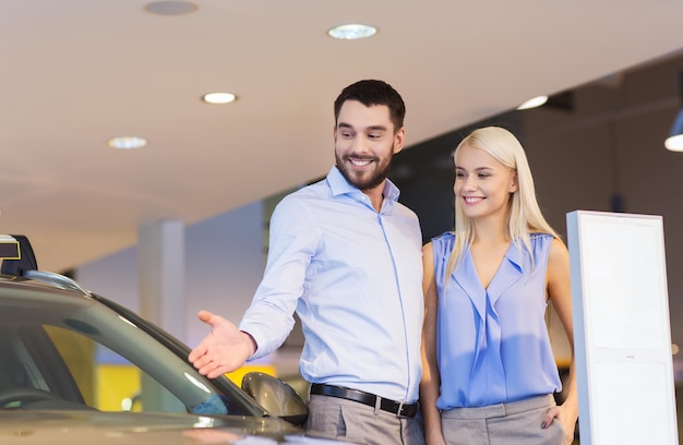 autogeschäft, autoverkauf, konsum und personenkonzept - glückliches paar, das auto in der autoshow oder im salon kauft