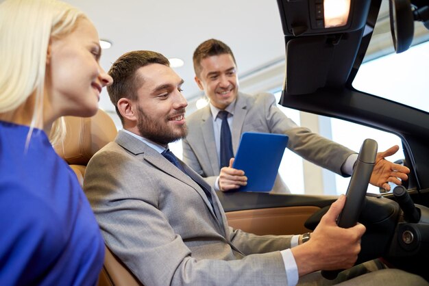 autogeschäft, autoverkauf, konsum und personenkonzept - glückliches paar mit autohändler in autoshow oder salon