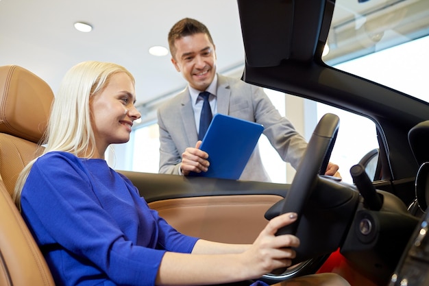 autogeschäft, autoverkauf, technologie und personenkonzept - glückliche frau und autohändler mit tablet-pc-computer in der autoshow oder im salon