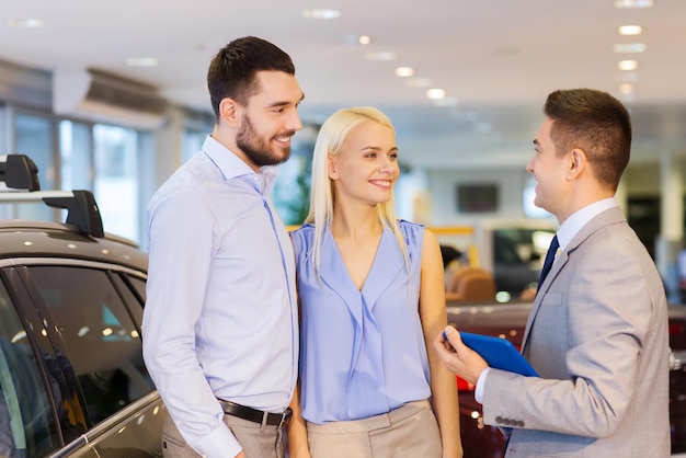 autogeschäft, autoverkauf, technologie und personenkonzept - glückliches paar mit autohändler in autoshow oder salon