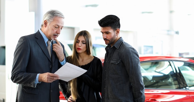 Autohändler, der einen Vertrag zu einem Paar in einem Autosalon liest