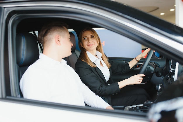 Autohaus besuchen. Schönes Paar schaut in die Kamera und lächelt, während es in ihrem neuen Auto sitzt