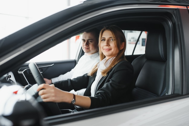 Autohaus besuchen. Schönes Paar schaut in die Kamera und lächelt, während es in ihrem neuen Auto sitzt