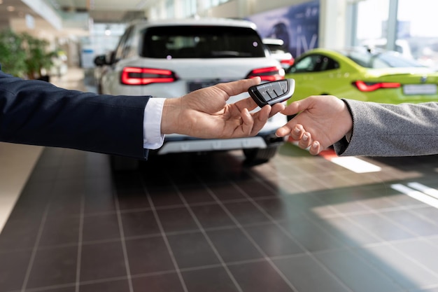 Autohausberater, der dem Käufer die Schlüssel vor dem Hintergrund neuer Autos überreicht