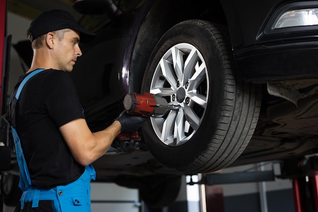 Automechaniker, der das Autorad eines angehobenen Autos bei der Montage der Reparaturwerkstatt ersetzt