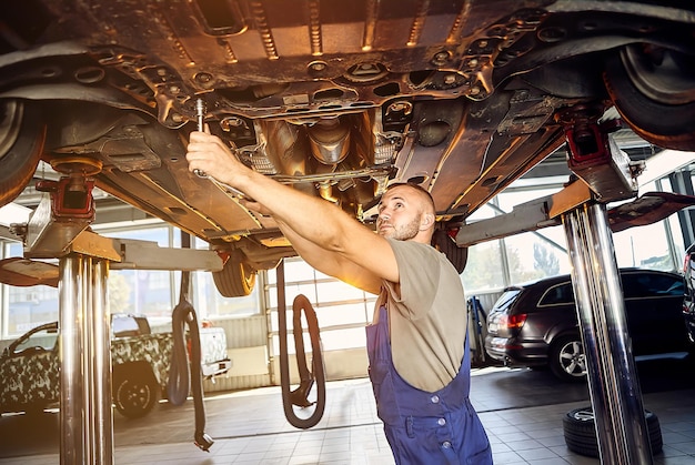Automechaniker, der das Fahrwerk des Automobils an der Tankstelle überprüft Männliche Arbeiter beheben Probleme mit dem Auto Fahrzeugwartungskonzept