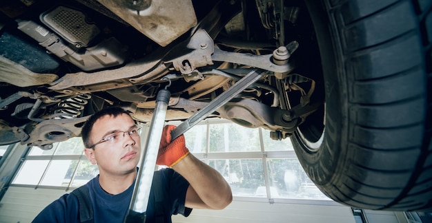 Automechaniker, der die Autoaufhängung des angehobenen Automobils an der Reparatur-Tankstelle untersucht