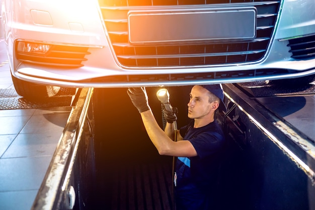 Automechaniker, der die Autoaufhängung des angehobenen Automobils an der Reparatur-Tankstelle untersucht.