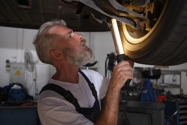 Automechaniker, der eine Lampe hält und die Räder eines Autos auf dem Aufzug untersucht