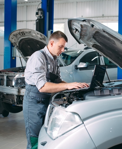 Automechaniker, der einen Computer-Laptop verwendet, um Automotorenteile zur Reparatur und Reparatur zu diagnostizieren und zu überprüfen.