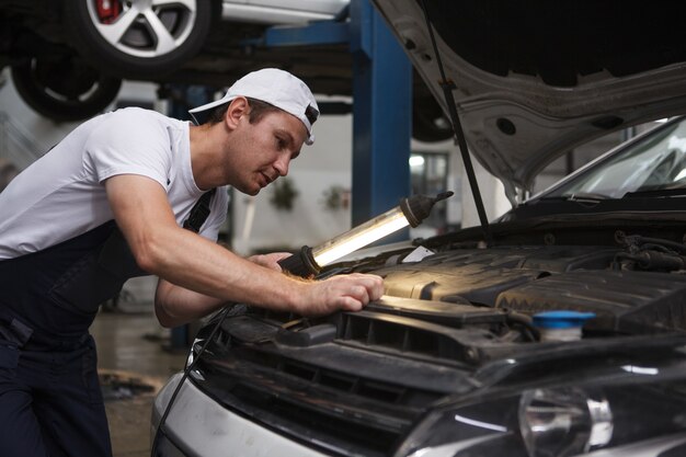 Automechaniker, der unter der Motorhaube eines Autos in seiner Garage schaut