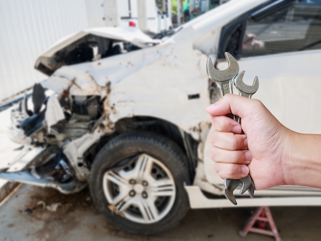 Automechaniker-Handhalteschlüssel mit Autounfall-Unfallschaden-Hintergrund-Karosserie-Reparaturkonzept