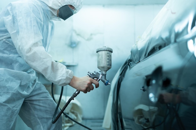 Automechaniker im Autosprühraum, der die Sprühdüse in die vordere Stoßstange des Autos einspritzt