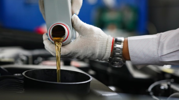 Automechaniker in Handschuhen gießen Motoröl in den Motor