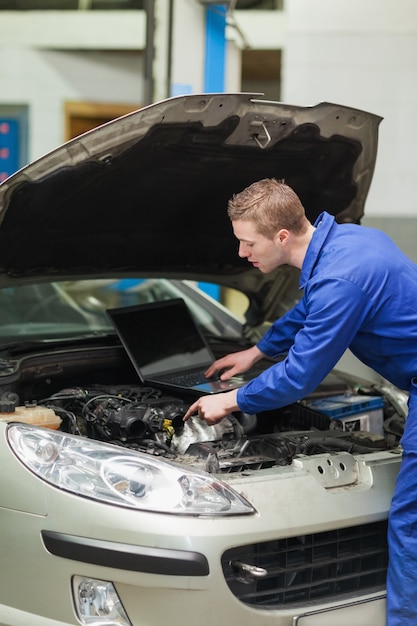 Automechaniker mit dem Laptop, der Auto repariert