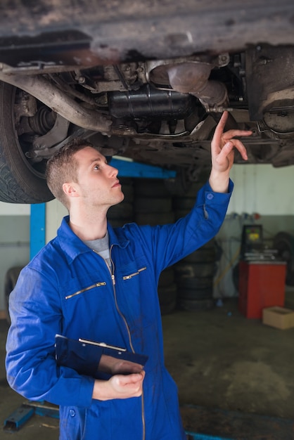 Automechaniker mit Klemmbrett unter Auto