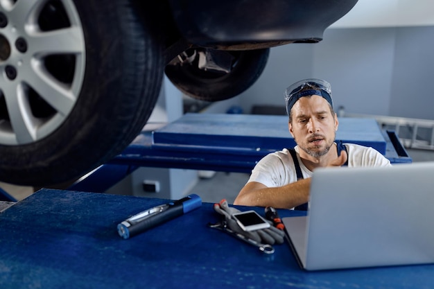 Automechaniker mit laptop bei der arbeit in der autowerkstatt