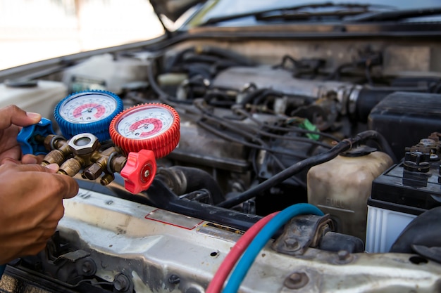 Automechaniker mit Messgerät zum Befüllen von Autoklimaanlagen.