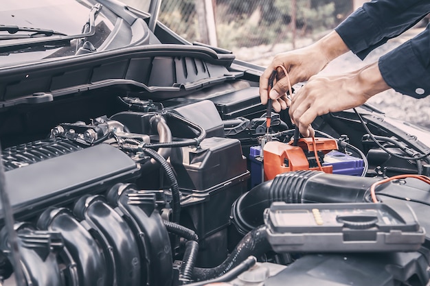 Automechaniker mit Messgerät zur Reparatur der Autobatterie