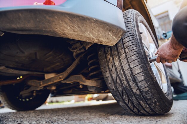 Automechaniker mit Werkzeug zum Reifenwechsel beim Hocken in der Werkstatt.