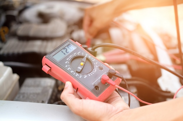 Automechaniker überprüfen Autobatteriespannung durch Voltmeter-Multimeter