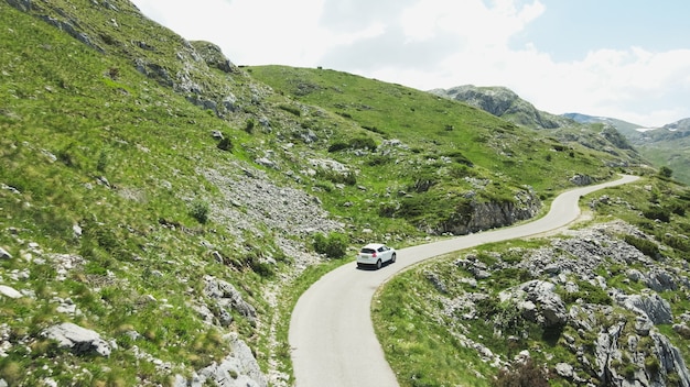 Foto un automóvil blanco recorre la hermosa carretera verde de la montaña en montenegro. aéreo