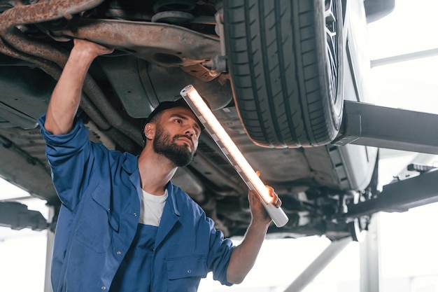 Bajo el automóvil utilizando un dispositivo de iluminación Mecánico de automóviles que trabaja en el garaje Servicio de reparación