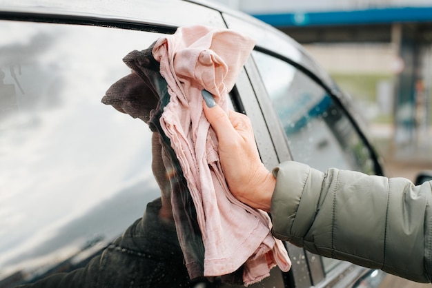 Autopflegekonzept Weibliche kaukasische Hand, die nach dem Waschen nasses, sauberes Fenster der Autotür mit Lappen reibt Nahaufnahme Seitenansicht