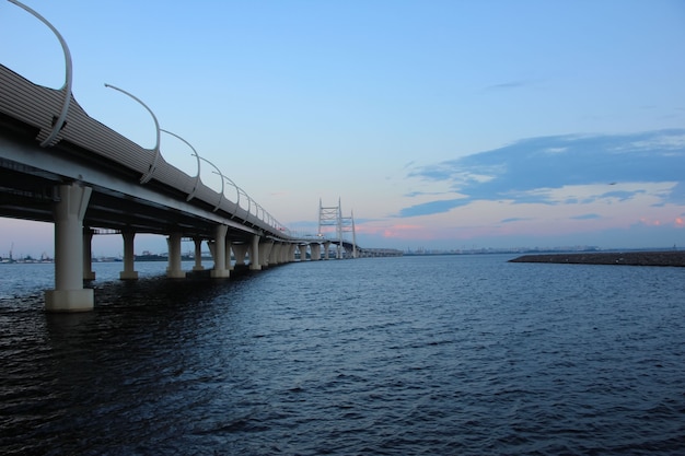 Autopista sobre la bahía y el puente del cable contra el cielo nocturno con reflejos rojos del sol poniente