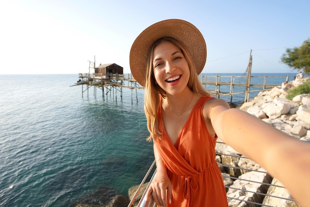 Autorretrato ao pôr do sol de uma mulher sorridente com máquina de pesca tradicional trabucco no fundo