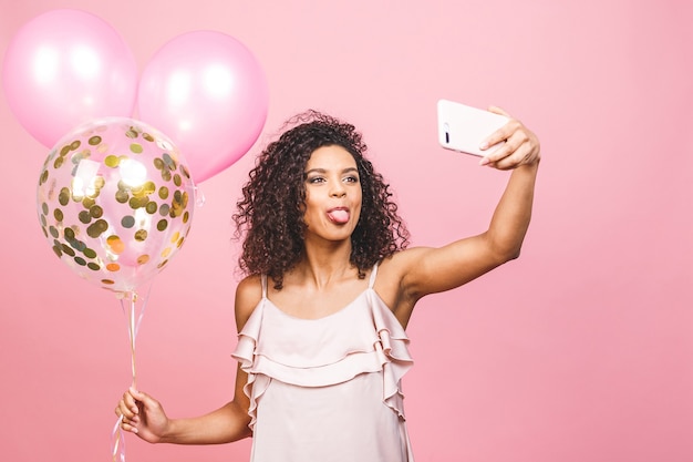 Autorretrato de niña afroamericana positiva en vestido con globos en la mano disparando selfie