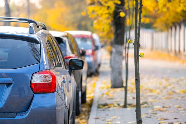 Autos, die an einem hellen Herbsttag in einer Reihe auf einer Straßenseite der Stadt geparkt sind.