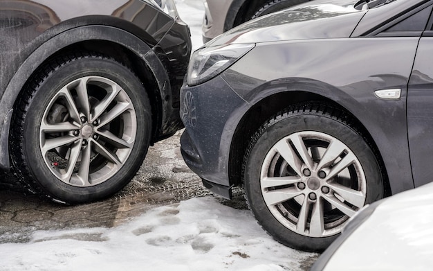 Autos estacionados con parachoques cerca uno del otro, detalle en el frente sucio y neumáticos en el suelo cubierto de nieve.