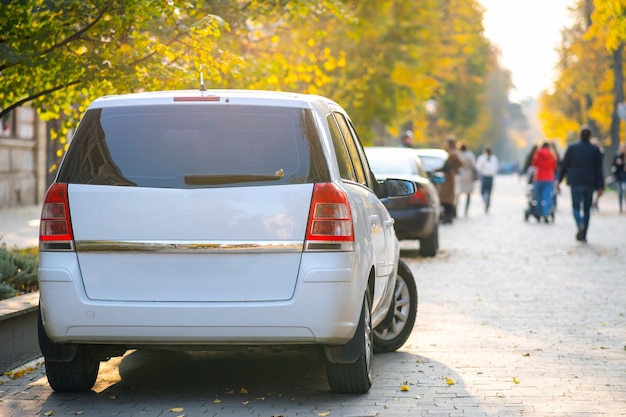 Autos parkten in einer Reihe auf einer Straßenseite der Stadt an einem hellen Herbsttag mit verschwommenen Leuten, die auf Fußgängerzone gehen.