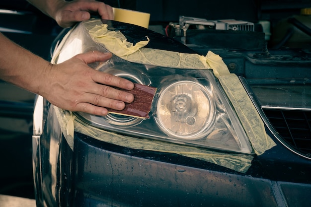 Autoscheinwerfer reinigen. der Meister reinigt die Scheinwerfer mit feinem Schleifpapier.