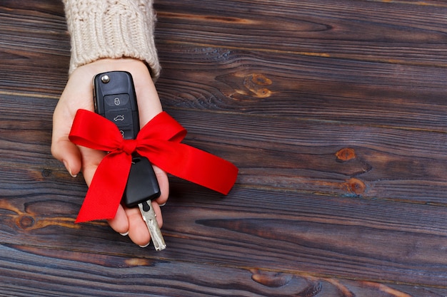 Autoschlüssel mit rotem Bogen in der woomen Hand auf hölzernem Hintergrund. Valentinstag-Konzept