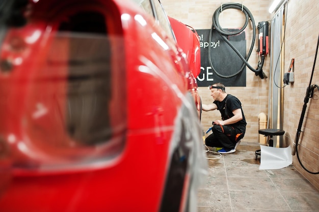 Foto autoservice-mitarbeiter legten in der fahrzeugwerkstatt eine rote karosserie mit anti-kies-folie an autoschutz mit spezialfolien