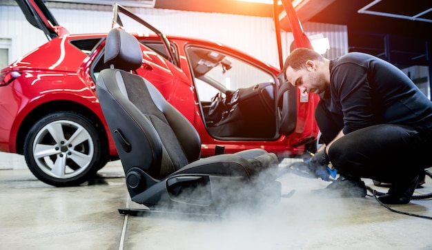 Autoservice-Mitarbeiter reinigen Autositz mit einem Dampfreiniger