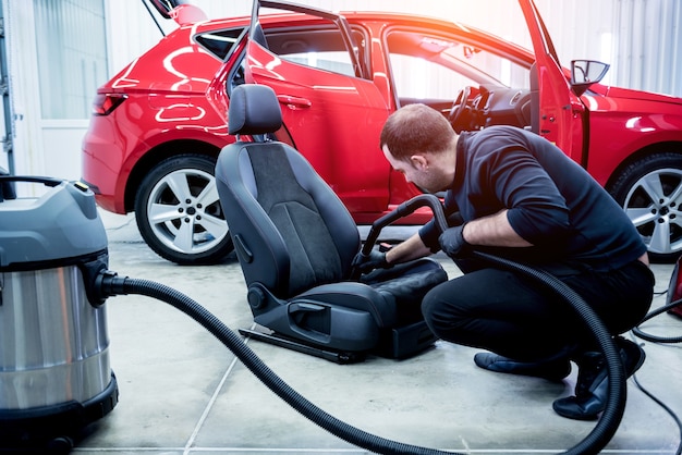 Autoservice-Mitarbeiter säubert Autositz mit Staubsauger