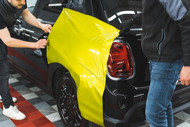 Foto autospezialisten bringen neongelbe vinylfolie auf der schwarzen autowerkstatt eines kunden an