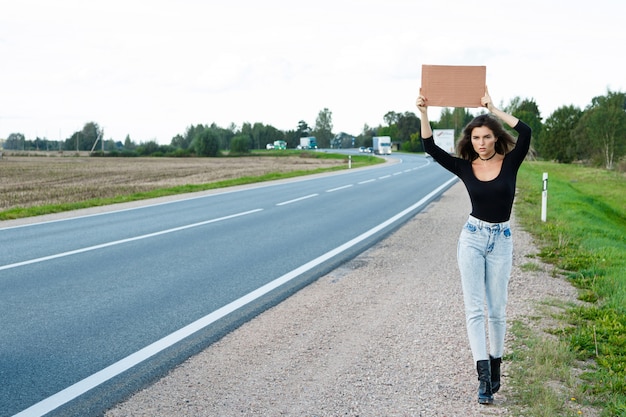 Foto autostopista en la carretera está sosteniendo un cartel de cartón en blanco